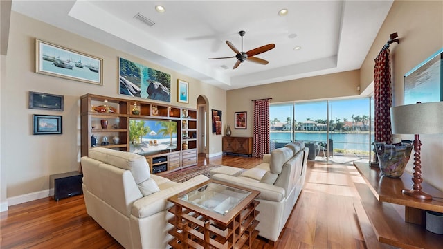 living room featuring a raised ceiling, ceiling fan, and wood-type flooring