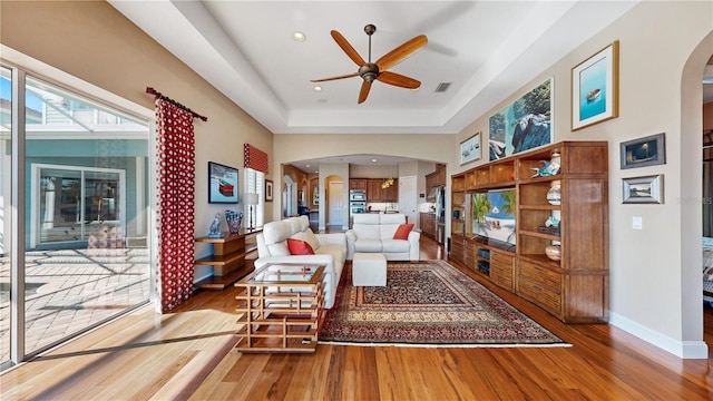 living room featuring hardwood / wood-style floors, ceiling fan, and a raised ceiling