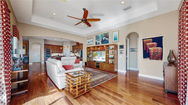 living room featuring a tray ceiling, ceiling fan, and hardwood / wood-style flooring