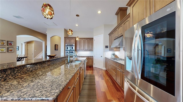 kitchen featuring dark wood-type flooring, a spacious island, dark stone countertops, appliances with stainless steel finishes, and decorative light fixtures