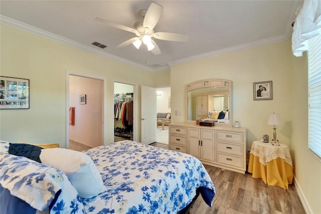 bedroom with ceiling fan, hardwood / wood-style floors, crown molding, a walk in closet, and a closet