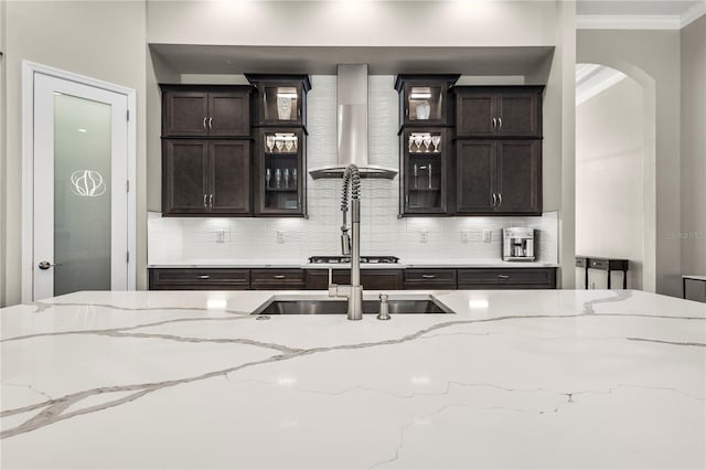 kitchen with wall chimney range hood, backsplash, crown molding, and light stone countertops