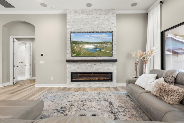 living room featuring light hardwood / wood-style flooring, a stone fireplace, and crown molding