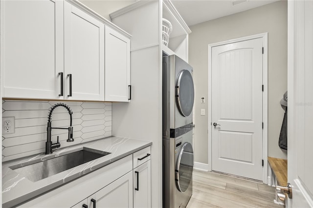 washroom with sink, cabinets, stacked washing maching and dryer, and light hardwood / wood-style flooring