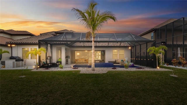 back house at dusk with a patio, glass enclosure, area for grilling, and a yard