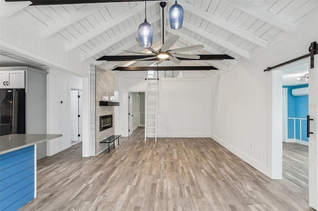 unfurnished living room with a barn door, an AC wall unit, light hardwood / wood-style flooring, ceiling fan, and lofted ceiling with beams