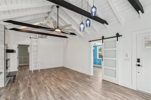 unfurnished living room featuring ceiling fan, lofted ceiling with beams, wood ceiling, a barn door, and hardwood / wood-style floors