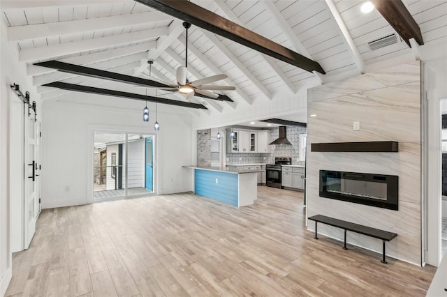 kitchen with wall chimney exhaust hood, backsplash, a barn door, stainless steel range, and light hardwood / wood-style floors