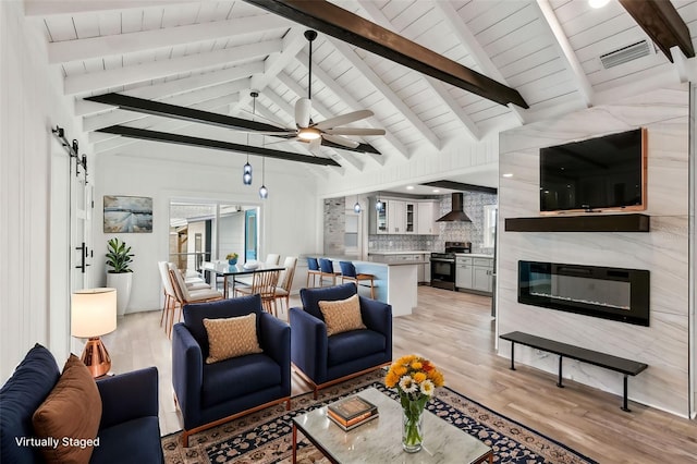 living room with a fireplace, a barn door, light hardwood / wood-style flooring, ceiling fan, and lofted ceiling with beams