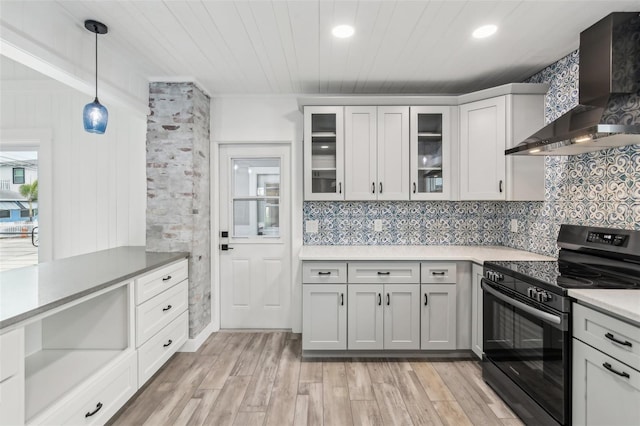 kitchen with hanging light fixtures, wall chimney exhaust hood, light wood-type flooring, white cabinetry, and electric range oven