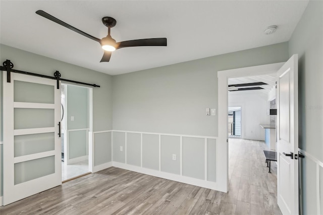 empty room featuring ceiling fan, a barn door, and light wood-type flooring