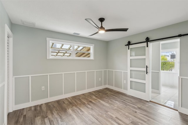 spare room featuring light hardwood / wood-style floors, ceiling fan, and a barn door