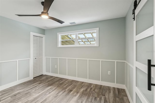 spare room featuring light hardwood / wood-style flooring, ceiling fan, and a barn door