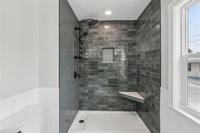 bathroom with a textured ceiling, tiled shower, and a wealth of natural light