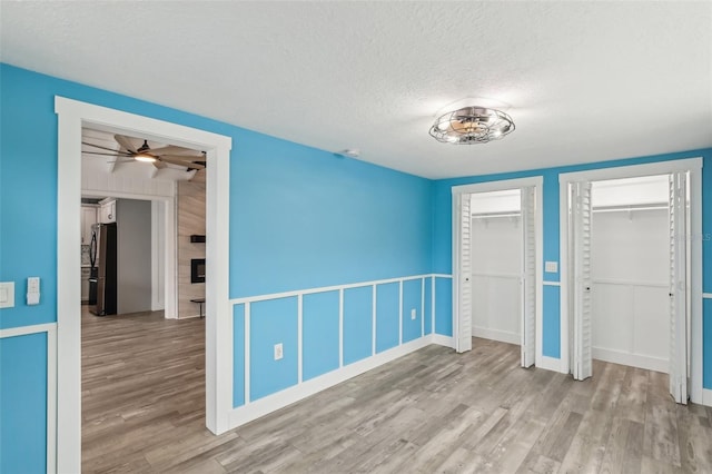 unfurnished bedroom with light hardwood / wood-style floors, two closets, a textured ceiling, and black fridge