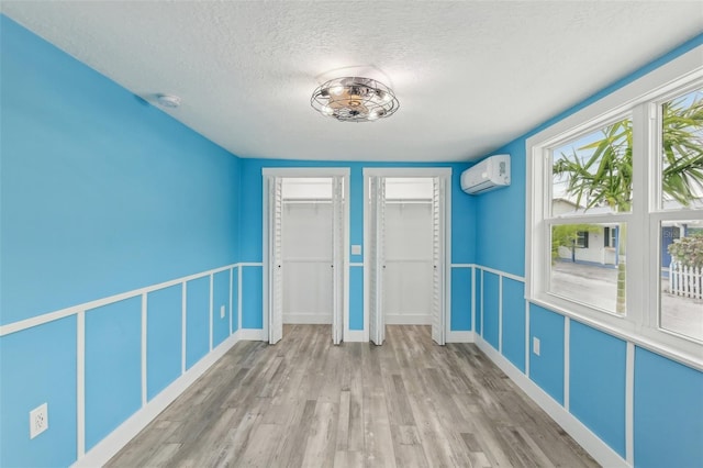 unfurnished bedroom with two closets, wood-type flooring, a textured ceiling, and a wall mounted AC