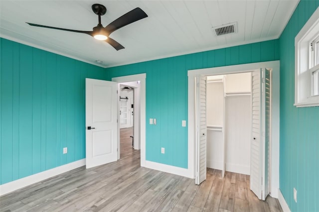 unfurnished bedroom with crown molding, light wood-type flooring, a closet, and ceiling fan