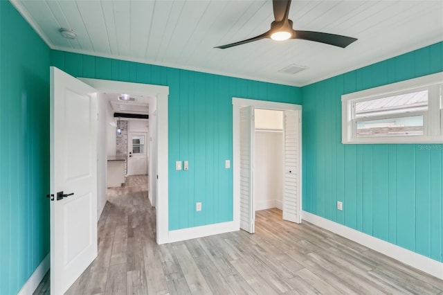 unfurnished bedroom with a walk in closet, light hardwood / wood-style floors, a closet, ceiling fan, and crown molding