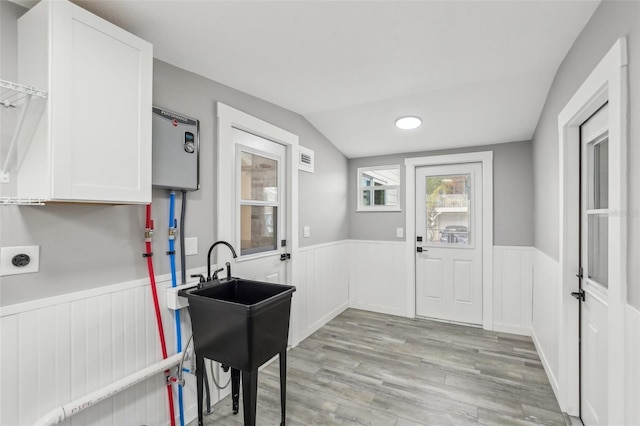 kitchen with vaulted ceiling, white cabinetry, and light hardwood / wood-style floors