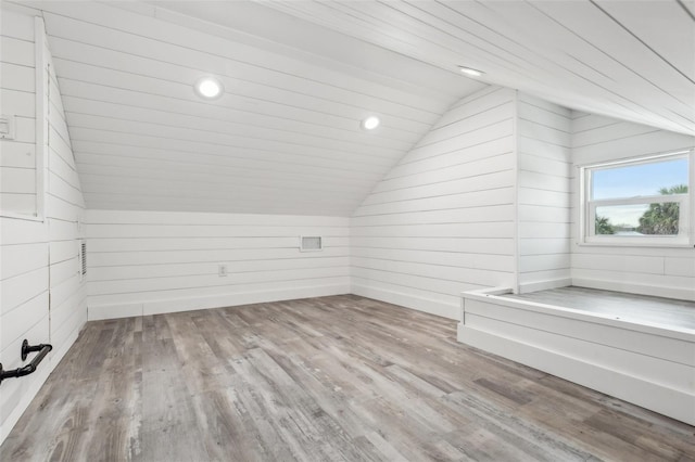 bonus room featuring vaulted ceiling, wood walls, and light hardwood / wood-style floors