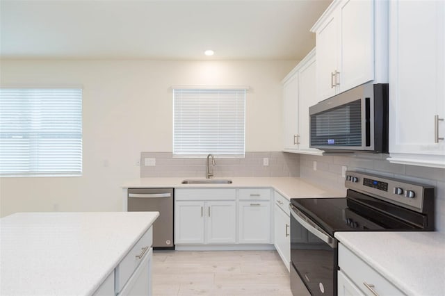 kitchen featuring sink, light hardwood / wood-style flooring, white cabinetry, backsplash, and stainless steel appliances