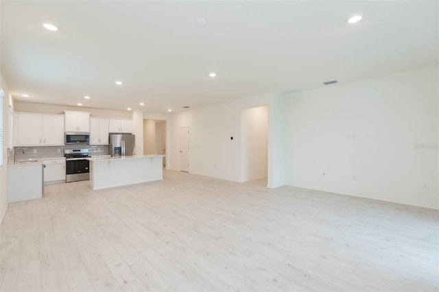 kitchen with sink, white cabinetry, light wood-type flooring, appliances with stainless steel finishes, and backsplash