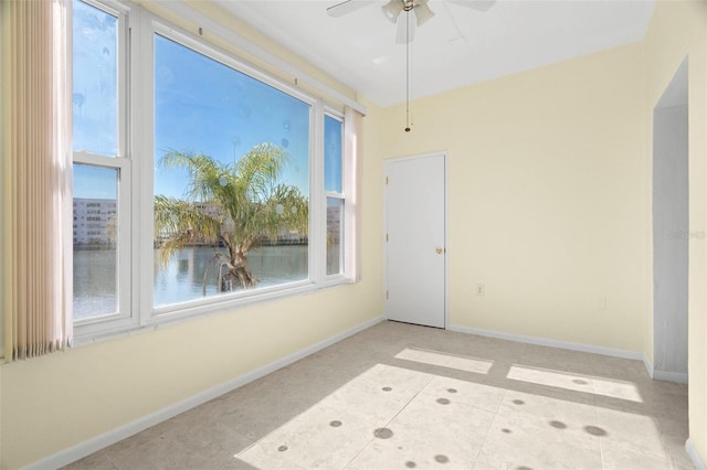 tiled spare room featuring ceiling fan, a healthy amount of sunlight, and a water view