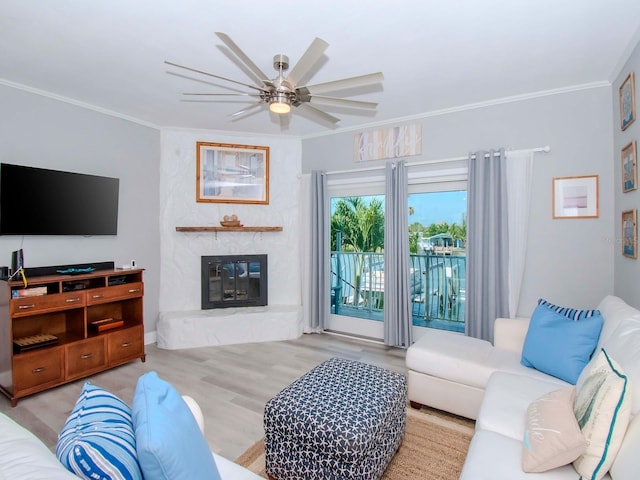 living room featuring ceiling fan, crown molding, light hardwood / wood-style flooring, and a stone fireplace