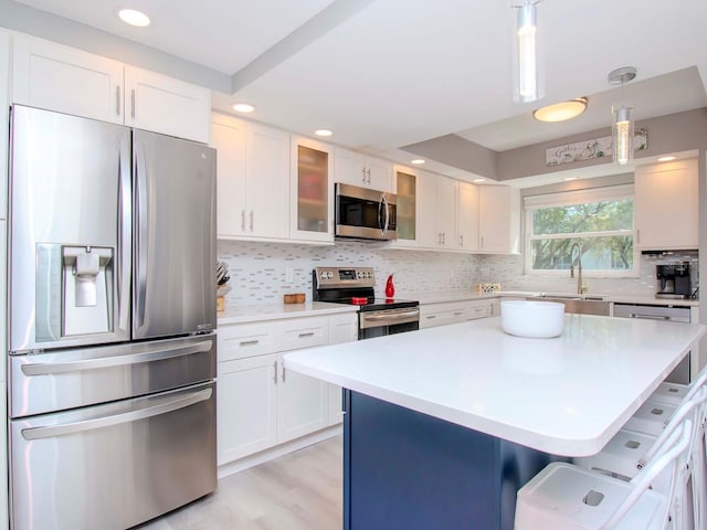 kitchen with a kitchen bar, sink, hanging light fixtures, appliances with stainless steel finishes, and white cabinets