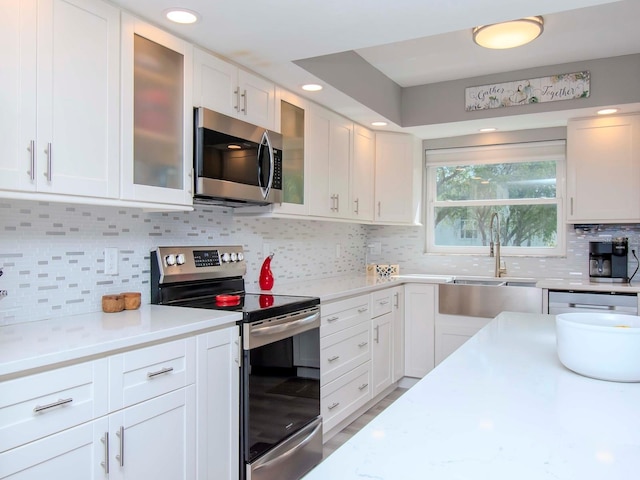 kitchen featuring decorative backsplash, sink, stainless steel appliances, white cabinets, and light stone counters