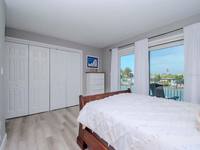 bedroom with a water view, access to exterior, and light hardwood / wood-style flooring