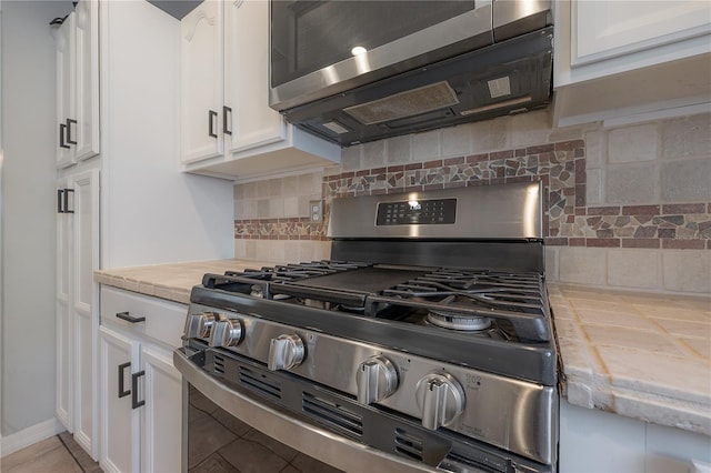 kitchen with decorative backsplash, light tile patterned flooring, white cabinets, and stainless steel gas stove