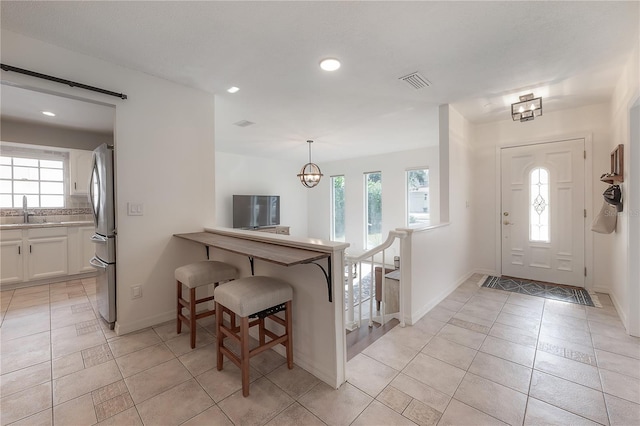 entrance foyer featuring a healthy amount of sunlight, sink, light tile patterned floors, and a notable chandelier