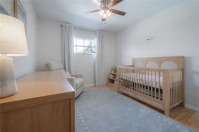 bedroom with a crib, light hardwood / wood-style floors, and ceiling fan