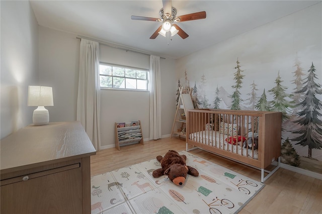 bedroom featuring a nursery area, ceiling fan, and light wood-type flooring