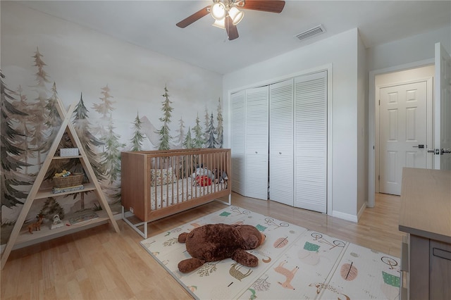 unfurnished bedroom with a crib, light hardwood / wood-style flooring, ceiling fan, and a closet