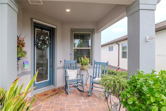 entrance to property featuring visible vents, a porch, and stucco siding