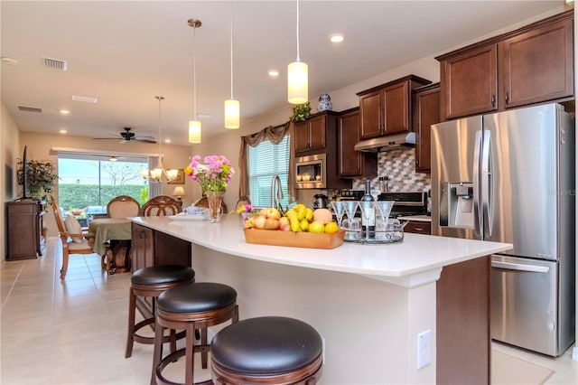 kitchen featuring stainless steel appliances, hanging light fixtures, light countertops, and a kitchen breakfast bar