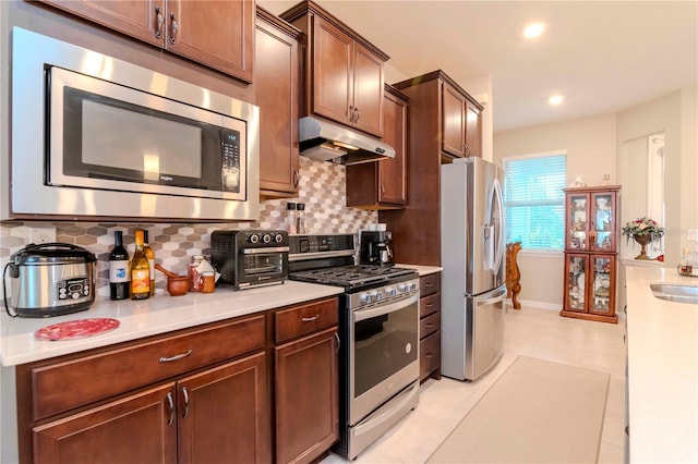 kitchen with a toaster, decorative backsplash, appliances with stainless steel finishes, light countertops, and under cabinet range hood