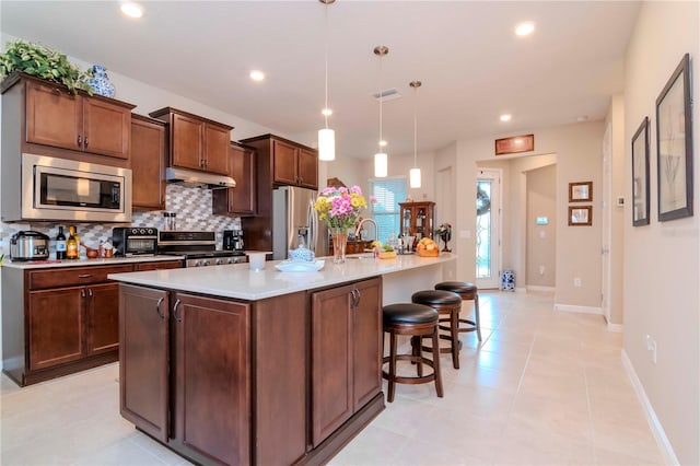 kitchen featuring hanging light fixtures, stainless steel appliances, light countertops, under cabinet range hood, and backsplash