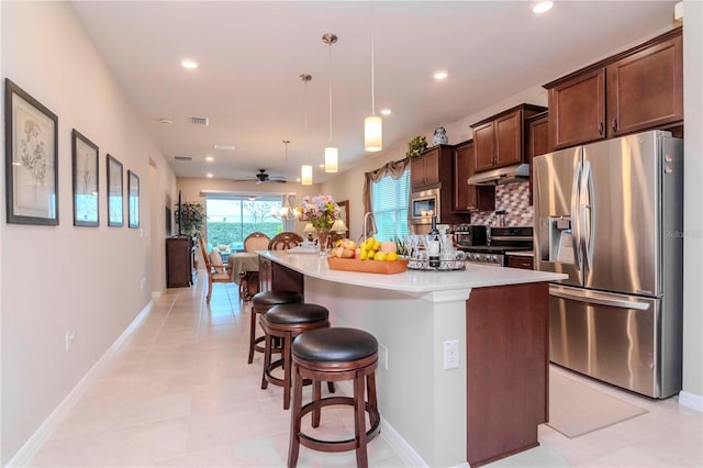 kitchen featuring a center island with sink, appliances with stainless steel finishes, a breakfast bar area, decorative light fixtures, and light countertops