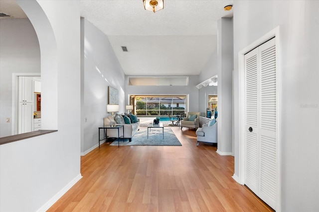 hallway featuring baseboards, visible vents, arched walkways, wood finished floors, and a textured ceiling