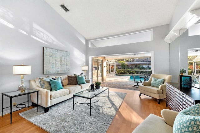 living room with high vaulted ceiling, a sunroom, visible vents, and wood finished floors