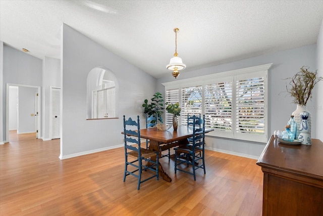 dining room featuring light wood-style flooring, baseboards, vaulted ceiling, and a textured ceiling