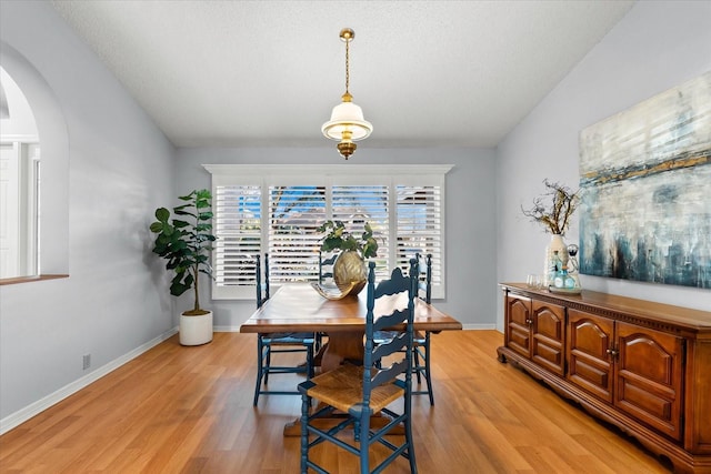 dining space with light wood-style floors, baseboards, arched walkways, and a textured ceiling