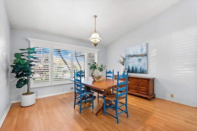 dining room with vaulted ceiling, a textured ceiling, light wood-type flooring, and baseboards