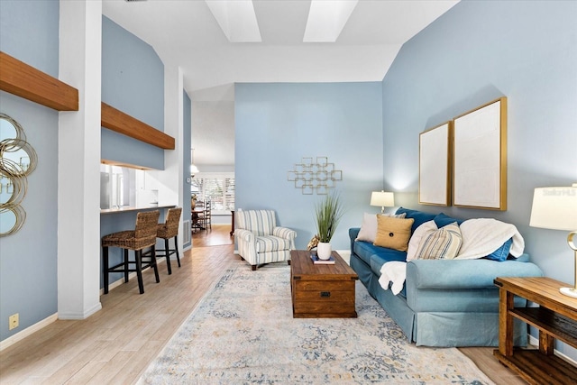 living area with vaulted ceiling with skylight, baseboards, and wood finished floors