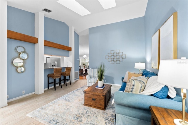 living room with lofted ceiling with skylight, wood finished floors, visible vents, and baseboards