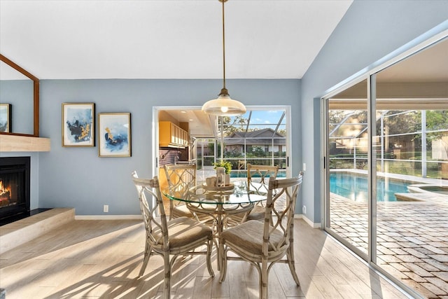 dining area with a warm lit fireplace, baseboards, a wealth of natural light, and light wood-style floors