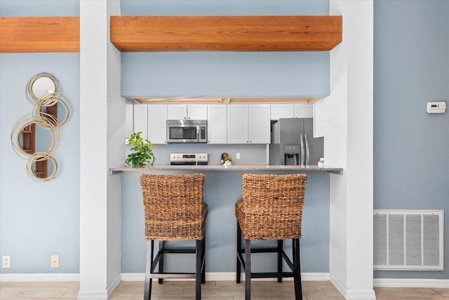 kitchen with a breakfast bar, visible vents, white cabinets, baseboards, and appliances with stainless steel finishes